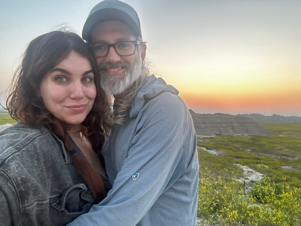 Steve and Nichole embracing at sunset above a green valley